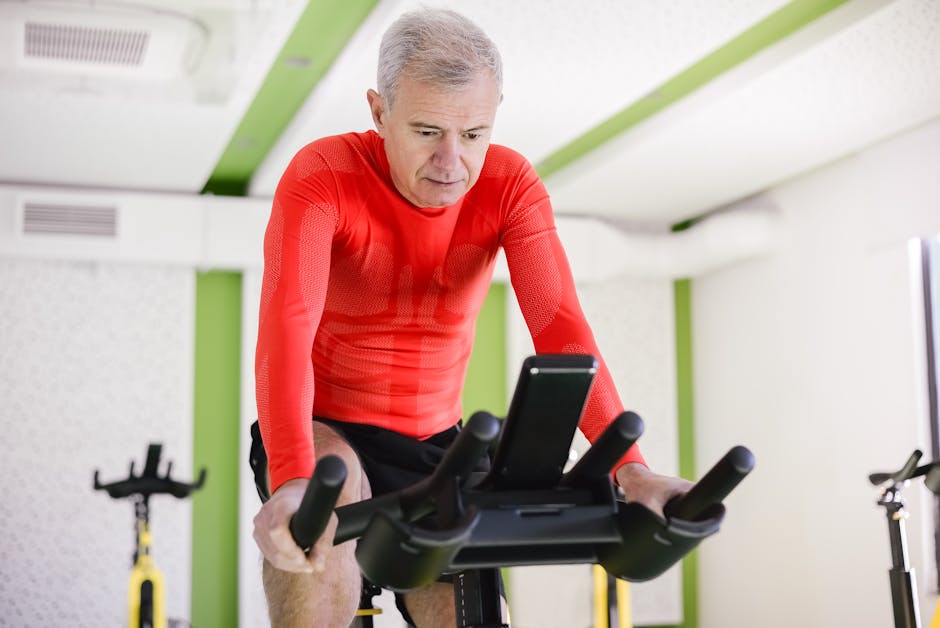 Senior man in red activewear exercising on stationary bike indoors, promoting healthy lifestyle