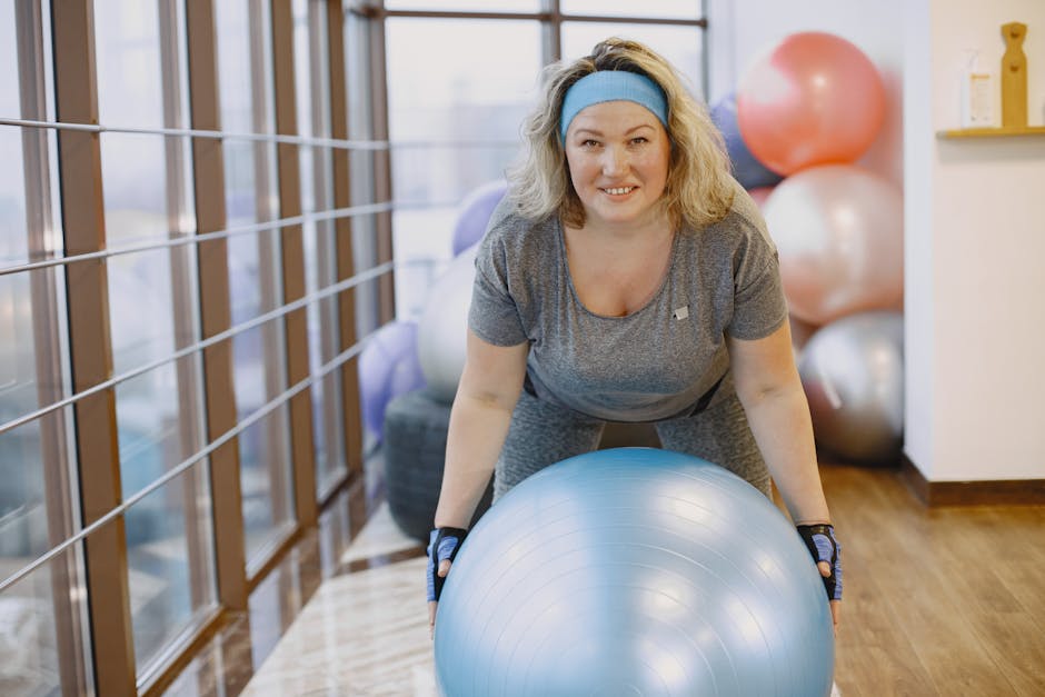 An adult woman engaging in a fitness workout with an exercise ball in a gym setting